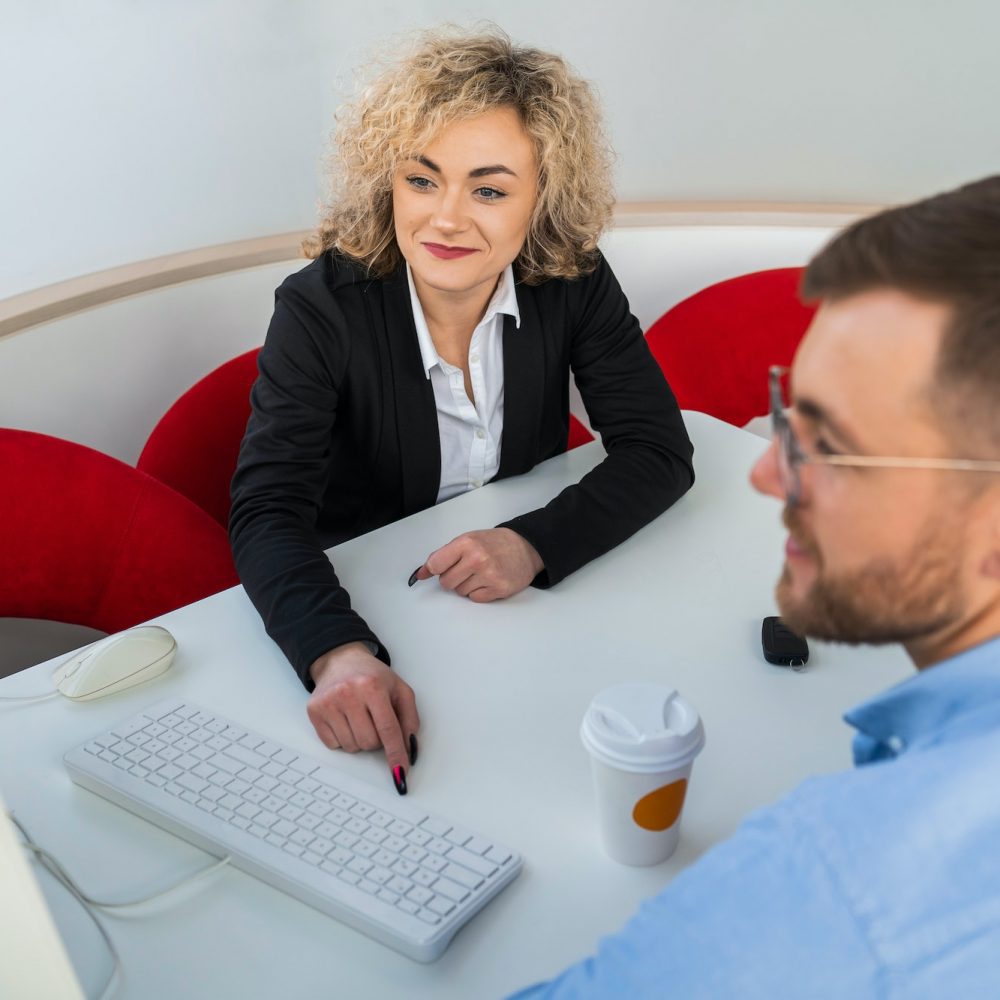 Car dealership manager with client at computer in showroom